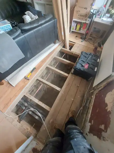 Floorboards lifted along a room with new pipework being run beneath them