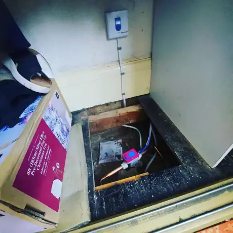 A lifted floor hatch with pipework running beneath the boards