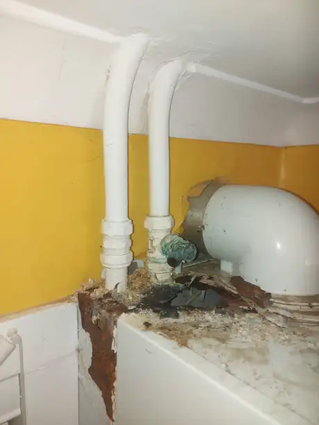 Pipework behind a bath with water damage to the wall and floor