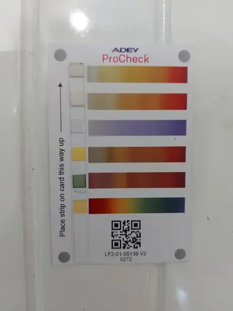 An ADEY ProCheck water test card held against the colour chart