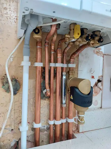 Copper pipework run across a brick wall to a boiler filter