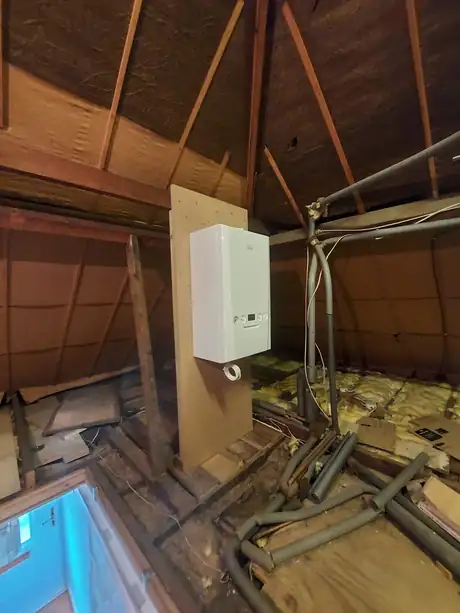 A boiler and pipework fitted in a loft with the floor open