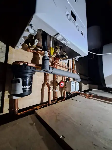 The underside of a boiler in a loft with the filter and pipework fitted