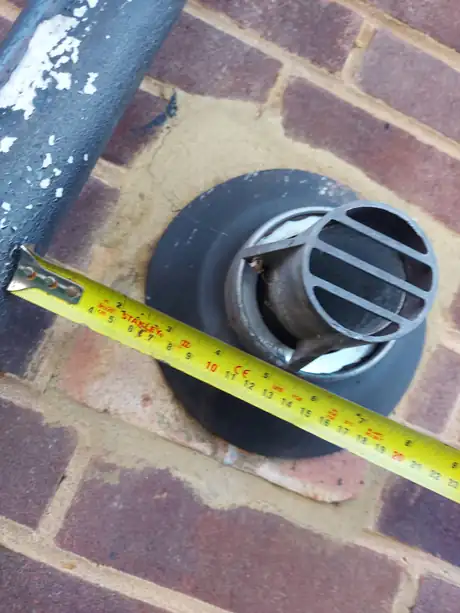 A flue terminal measured against the brickwork with a tape