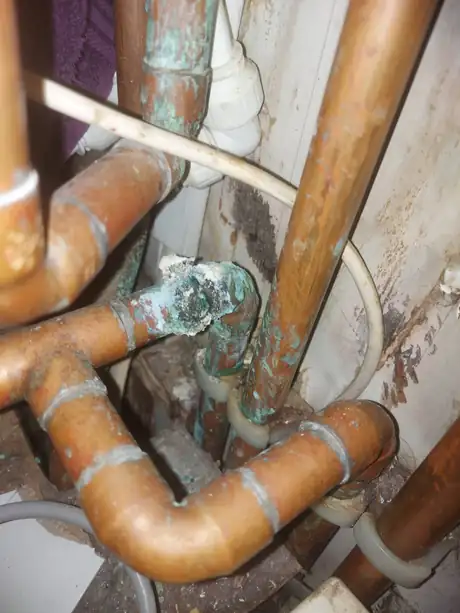 Corroded copper pipework showing green verdigris at the joints