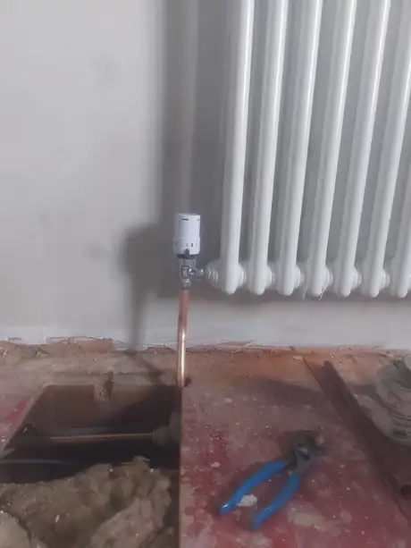 A column radiator being fitted with the pipe brought up through the floor