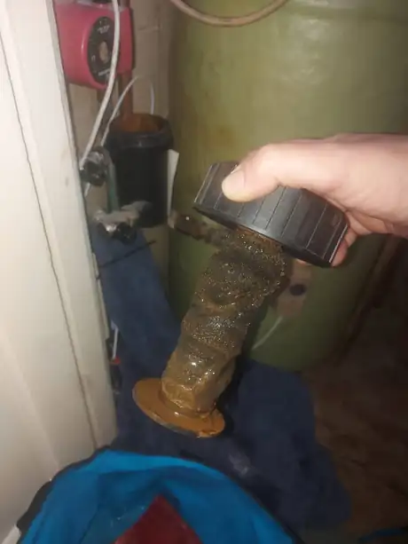 An immersion heater covered in thick limescale, held in the hand