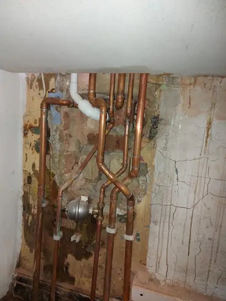 Copper pipework and an expansion vessel on a stripped wall