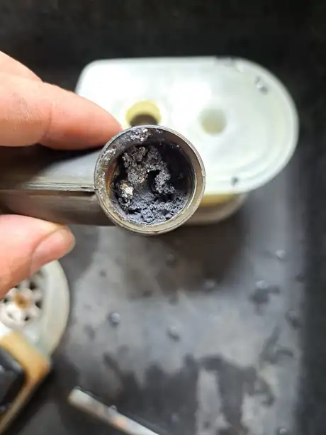 The open end of a pipe blocked with debris, held in the hand