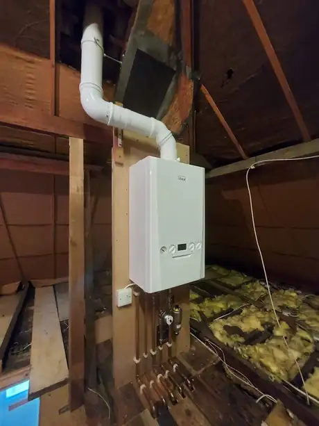 A boiler fitted in a loft with its flue and pipework