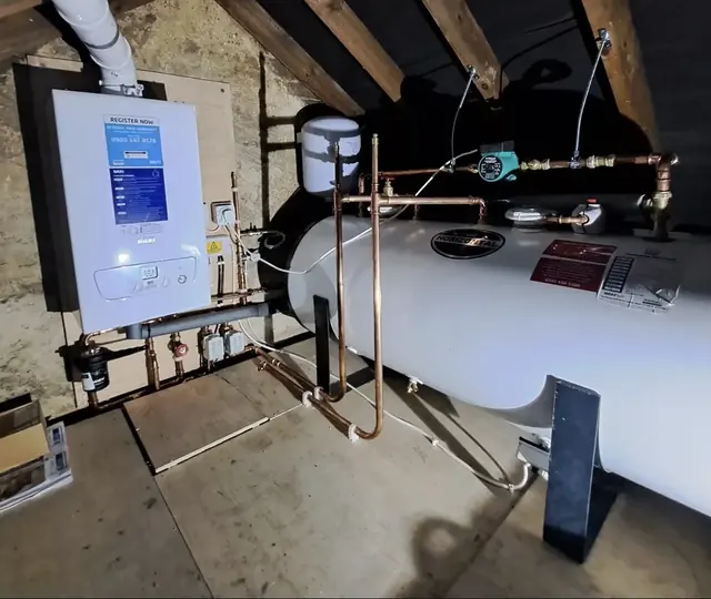 A boiler and hot water cylinder fitted in a loft, with the copper pipework run and clipped along the joists