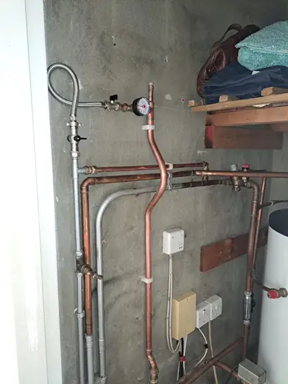 Copper and steel pipework, a pressure gauge and a hot water cylinder in an airing cupboard
