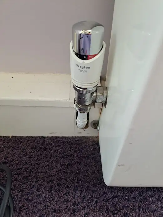 A thermostatic radiator valve fitted to the bottom of a radiator, with the pipe run up through the skirting board